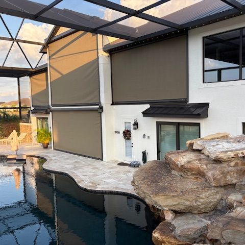 A pool lanai with a motorized screen lowered beside a rock waterfall