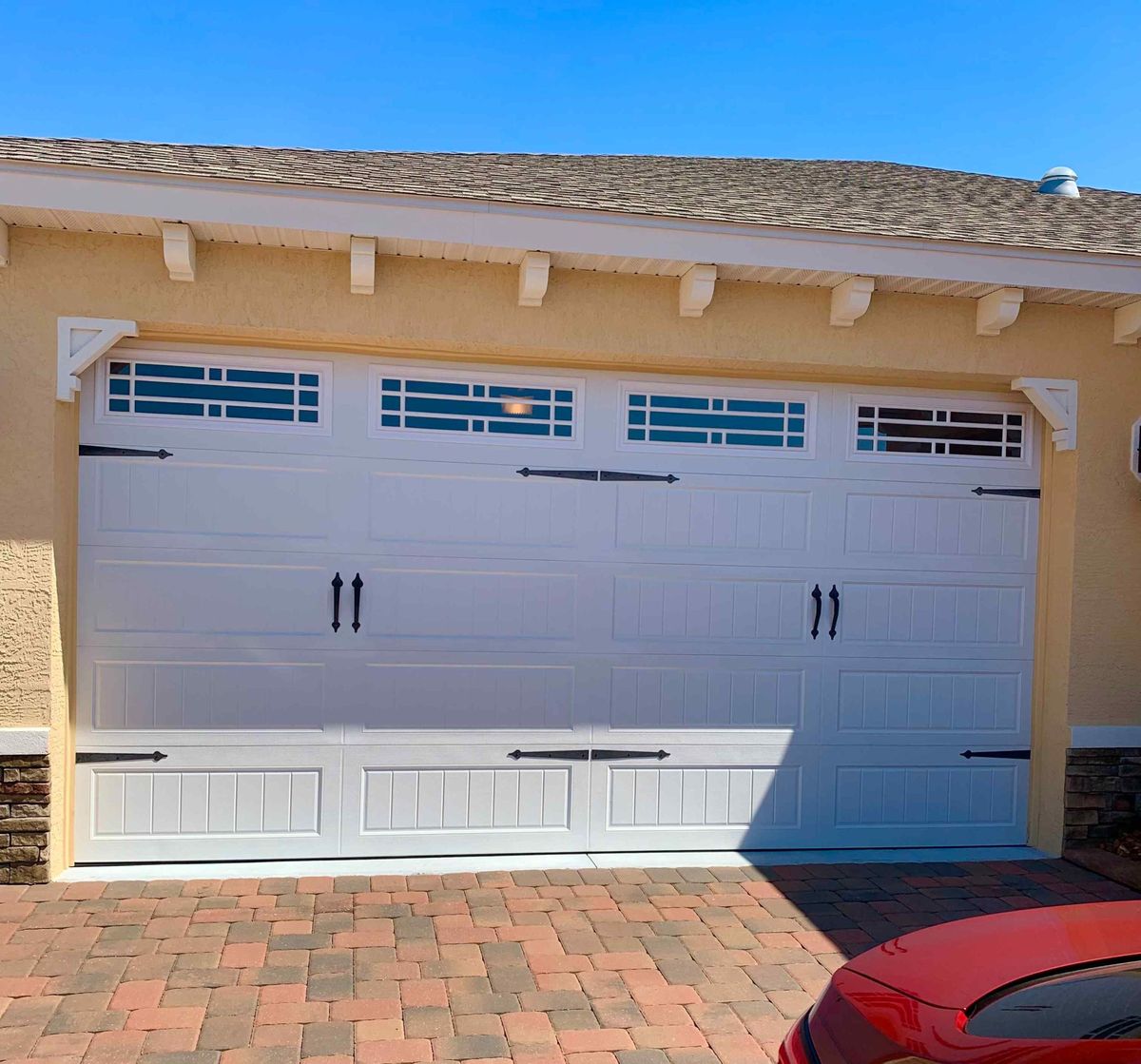 A new white carriage-style garage door above a brick paver driveway