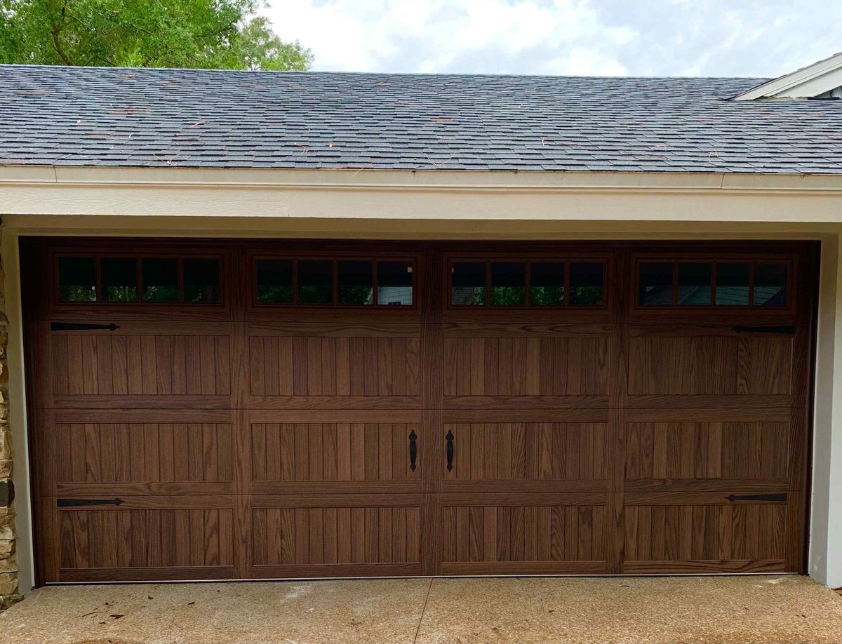 A wood-look garage door with a column of dark window panels on a tan home
